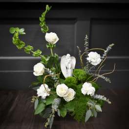 White roses and carnations arranged with greenery and a small angel figurine