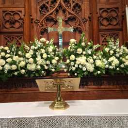 White floral arrangements flank a church altar with a cross.