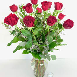Red roses arranged in a clear glass vase with greenery