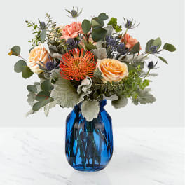 Mixed bouquet in a blue glass vase with peach and orange blooms