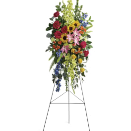 Tall standing floral spray with roses, lilies, sunflowers, and blue flowers on an easel