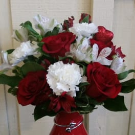 Red roses and white carnations in a red vase with a glittery heart pick