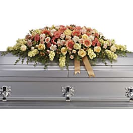 Large floral spray on a silver casket with peach and cream flowers
