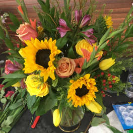 Mixed bouquet with sunflowers, roses, and tulips in a glass vase