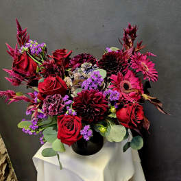Red roses and magenta flowers arranged in a black vase