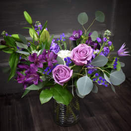 Purple roses and mixed purple flowers in a glass vase