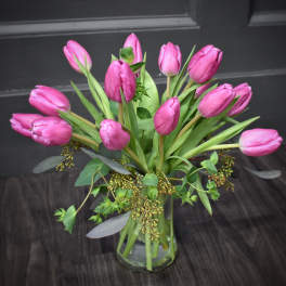 Pink tulips arranged in a clear glass vase with mixed greenery