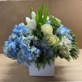 Blue hydrangeas and white roses arranged in a white square vase