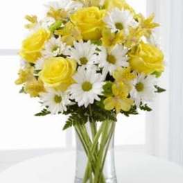 Arrangement of yellow roses, white daisies, and yellow blooms in a clear glass vase