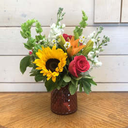 Bouquet of sunflowers, roses, lilies, and white blooms in a red vase