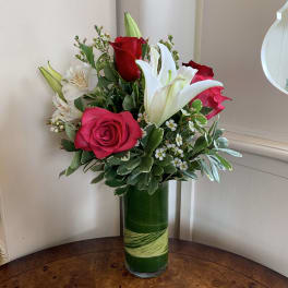 Red roses and white lilies in a tall green glass vase