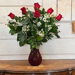 Red roses arranged in a burgundy vase with white filler flowers