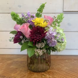 Mixed bouquet in a brown glass vase with pink, yellow, purple, and green flowers