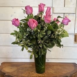 Pink roses arranged in a tall glass vase with greenery