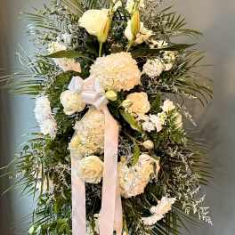 Tall white standing spray with roses, lilies, hydrangeas, and long white ribbons on an easel