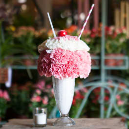 Pink and white carnations in a tall glass dessert glass with straws