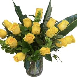 Yellow roses arranged in a clear glass vase with broad green leaves