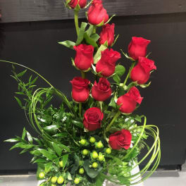 Tall arrangement of red roses with green filler in a white container