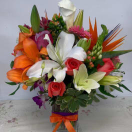 Colorful mixed bouquet in a square glass vase with lilies, roses, and orchids