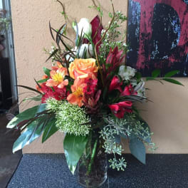 Tall mixed bouquet with orange roses and red lilies in a glass vase