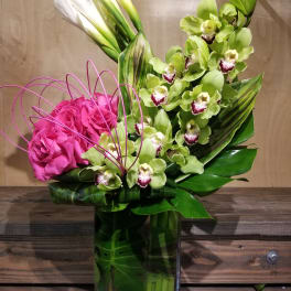 Pink roses and green orchids in a tall glass vase with white calla lilies