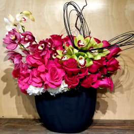 Pink roses and orchids arranged in a dark vase