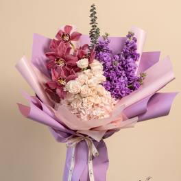 Bouquet of pink orchids, roses, and purple flowers wrapped in lavender paper