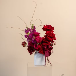 Red and pink rose arrangement in a white vase with curly branches