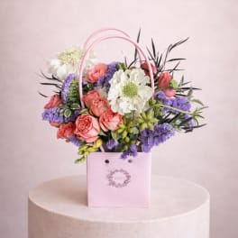 Pink basket arrangement with coral roses, white blooms, and purple flowers