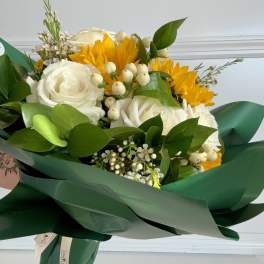 Bouquet of white roses and yellow sunflowers wrapped in dark green paper