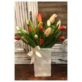 Bouquet of multicolored tulips in a white wrapped container with a ribbon