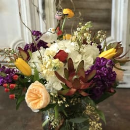 Mixed bouquet in a glass vase with yellow tulips, white hydrangea, and purple blooms