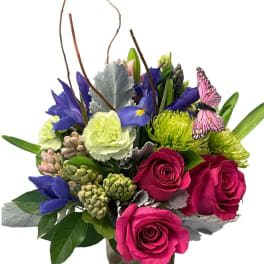 Mixed bouquet in a glass vase with roses, irises, and a butterfly accent