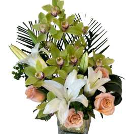 Orchid and lily arrangement with peach roses in a square glass vase