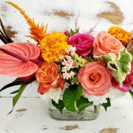 Bright mixed bouquet with roses, anthurium, and marigolds in a glass vase