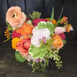Mixed bouquet of roses, orchids, and ranunculus in a glass vase