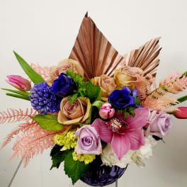 Bouquet of roses, orchids, and blue blooms in a purple vase