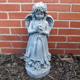 Blue-gray angel statue holding flowers in front of a brick wall
