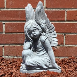 Gray angel statue of a seated child against a brick wall