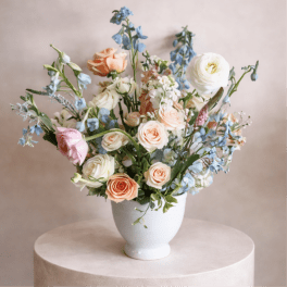 Pastel bouquet of roses and blue flowers in a white vase