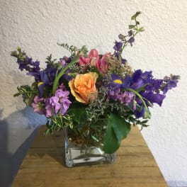 Mixed bouquet in a square glass vase with purple, pink, and orange flowers