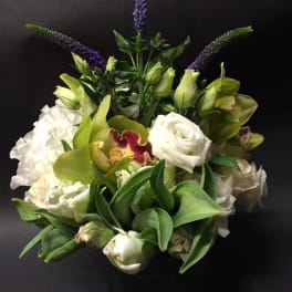White and green floral arrangement with purple spikes in a black vase