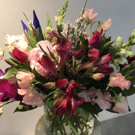 Mixed bouquet of pink, purple, and white flowers in a glass vase