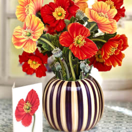 Bouquet of red and orange poppy-like flowers in a striped vase with a card