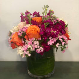 Mixed bouquet of orange roses, pink flowers, and white blooms in a glass vase