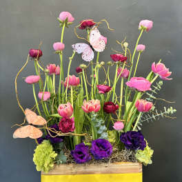 Tall pink and purple floral arrangement in a wooden box with butterflies