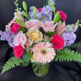 Mixed bouquet of pink, lavender, and yellow flowers in a glass vase
