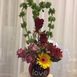 Mixed flower arrangement in a red vase with a tall green arch and "love" text