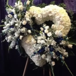 Large white floral funeral wreath on an easel with blue accents