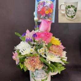 Colorful mixed flower arrangement in a white mug with floral print and an attached flower seed packet.
